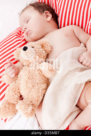 Mignon petit bébé à dormir sur le rouge et blanc oreiller avec ours Banque D'Images