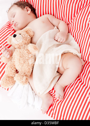 Mignon petit bébé à dormir sur le rouge et blanc oreiller avec ours Banque D'Images