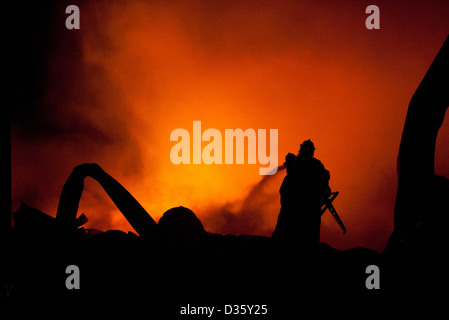 Silhouette de pompiers la lutte contre un feu faisant rage avec d'immenses flammes de bois brûlant Banque D'Images