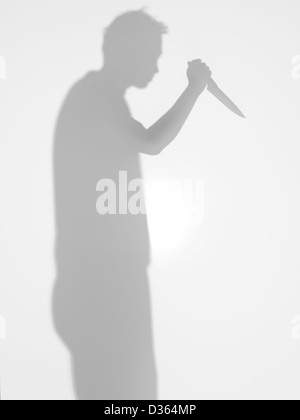 L'homme silhouette avec cuisine couteau à la main debout de profil, avec un geste d'attaquer quelqu'un, derrière une surfa Banque D'Images