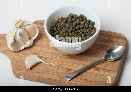 Caper Berries marinées dans du vinaigre sur une planche de bois avec la moitié d'un bulbe de l'ail frais. Banque D'Images