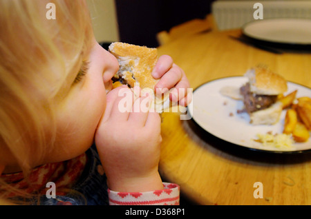 Une jeune fille mange un hamburger avec des frites et de la sauce tomate à la table pour son dîner Banque D'Images