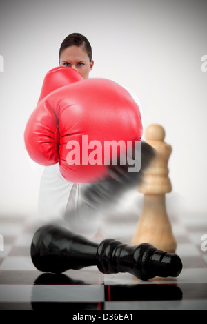 Woman in boxing gloves knocking over chess pieces Banque D'Images