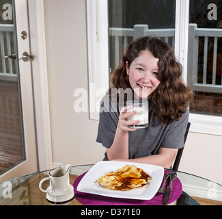 Jeune adolescente, boire du lait avec un grand sourire sur le visage et seul gros pancake sur plaque blanche avec le sirop d'érable sur le dessus Banque D'Images