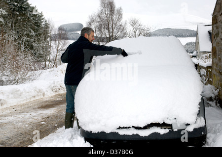 Un homme efface son pare-brise de voiture après une autre nuit de fortes chutes de neige dans l'Aberdeenshire en Écosse. Banque D'Images