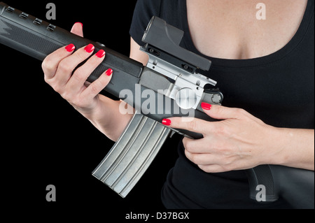 Femme avec de beaux ongles rouge tenant un fusil d'assaut noir et argent isolé sur noir. Banque D'Images