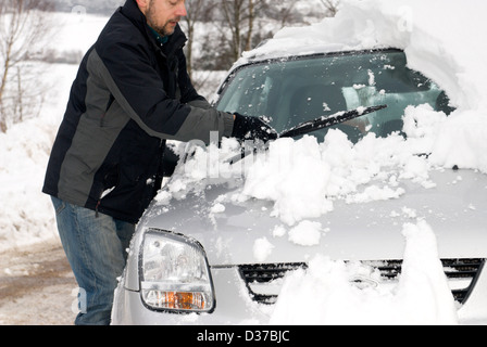 Un homme efface son pare-brise de voiture après une autre nuit de fortes chutes de neige dans l'Aberdeenshire en Écosse. Banque D'Images