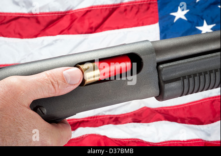 Un homme charge un fusil de shell dans un fusil de la pompe. Tourné contre un drapeau américain. Banque D'Images