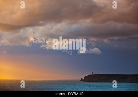 Stormy coucher de soleil sur l'océan Atlantique et les falaises du Cap St Vincent avec phare dans la distance Sagres Algarve Portugal Banque D'Images