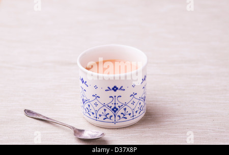 Tasse de Rooibos (buisson rouge) Thé au lait dans un service à la Chine avec une cuillère ancienne sur un fond neutre. Banque D'Images