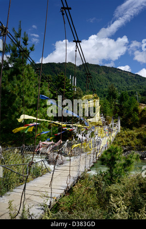 Pont bhoutanais couvert de drapeaux de prière traverse la rivière dans la vallée de Chokhor,Bumthang Bhoutan,,collines boisées derrière,36MPX,HI-RES Banque D'Images