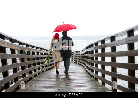 Couple en train de marcher sur la jetée en bois dans la pluie Banque D'Images