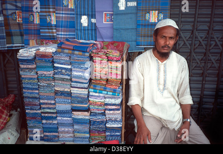 Vendeur de rue de ville assis à son stand de lunghi / sarong. Dhaka, Bangladesh Banque D'Images