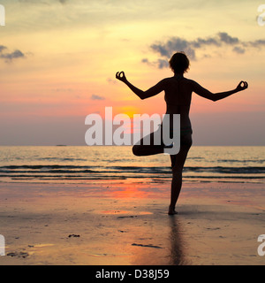 Yoga woman effectue un exercice sur la plage pendant le coucher du soleil, avec la réflexion dans l'eau