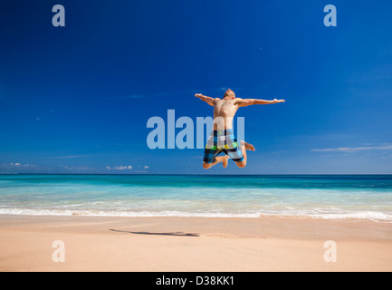 Jeune homme athlétique jouissant de l'été, sauter dans une plage tropicale Banque D'Images