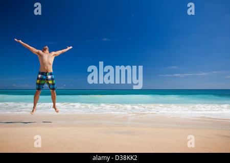 Jeune homme athlétique jouissant de l'été, sauter dans une plage tropicale Banque D'Images