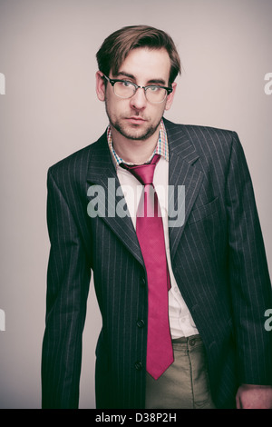 Businessman dans son 20s portant pinstripe veste de costume, chemise blanche, cravate rouge et verres se unimpressedly à huis clos. Banque D'Images