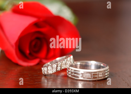 Deux anneaux de mariage avec une rose rouge posé sur une table Banque D'Images
