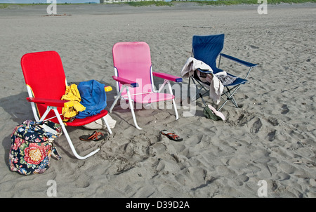 Trois de plage multicolores, avec divers objets laissés derrière la plage, vêtements, sandales, sacs, téléphones sur une plage de sable. Banque D'Images