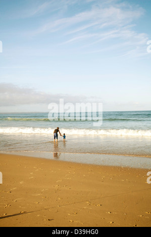La mère et le fils de la pagaie dans la mer sur la côte est de l'Australie avec des vagues et golden sands au coucher du soleil en fin d'après-midi. Banque D'Images