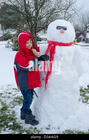 Garçon de six ans avec bonhomme de neige dans le jardin. Janvier, Royaume-Uni. Banque D'Images