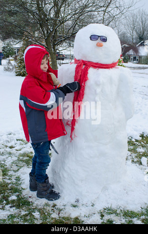 Garçon de six ans avec bonhomme de neige dans le jardin. Janvier, Royaume-Uni. Banque D'Images