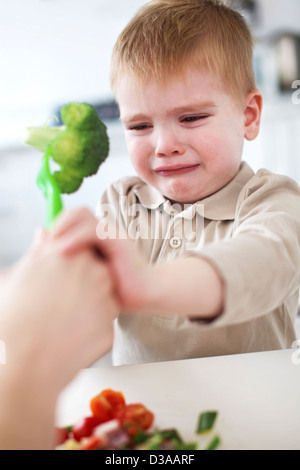 Crying boy refusant le brocoli dans la cuisine Banque D'Images