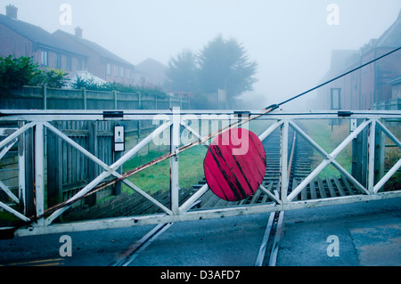 Passage à niveau à l'ancienne avec porte en bois rouge cercle et lignes de chemin de fer sur un jour humide de Misty en Angleterre. Banque D'Images