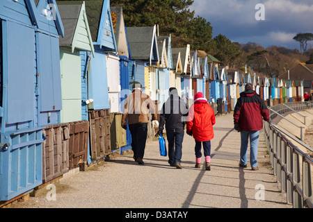 Les gens qui marchent le long de la promenade le long des huttes de plage à Avon Beach, Mudeford, Christchurch, Dorset UK en février Banque D'Images