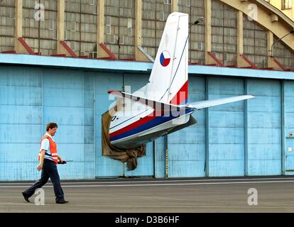 (Afp) - Un employé passe devant la queue d'un avion qui sort d'un hangar fermé sur la base aérienne militaire dans Prague-Bakerty, République tchèque, le 20 août 2002. L'avion a été portée à la base aérienne pour la maintenance, mais était trop grand pour tenir entièrement dans le hangar. Banque D'Images