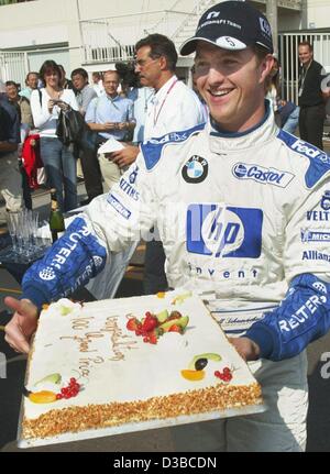 (Afp) - L'allemand Ralf Schumacher pilote de Formule 1 porte un gâteau au réfrigérateur avant le Grand Prix du Japon sur le cour de course à Suzuka, Japon, 13 octobre 2002. On lui a offert le gâteau en sport automobile directeur Mario Theissen (en arrière-plan) pour son 100e Grand Prix de départ. Banque D'Images