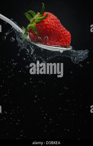 Cuillère à thé avec fraise et fuite d'eau minérale naturelle en noir au sol. Banque D'Images