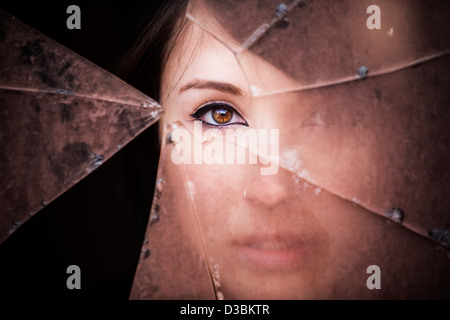 Femme regardant à travers le verre brisé sale Banque D'Images