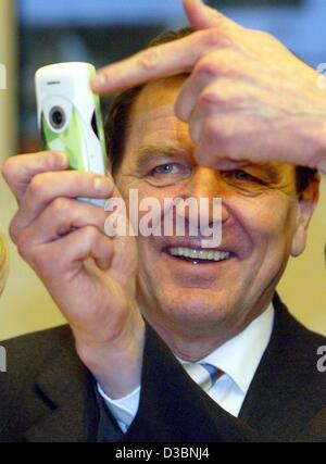 (Afp) - Le Chancelier allemand Gerhard Schroeder examine un nouveau téléphone mobile avec appareil photo intégré au stand de marché de Nokia, au plus grand salon informatique CeBIT à Hanovre, Allemagne, 12 mars 2003. Le CeBIT aura lieu du 12 au 19 mars 2003. Plus de 6 500 entreprises d'ar Banque D'Images