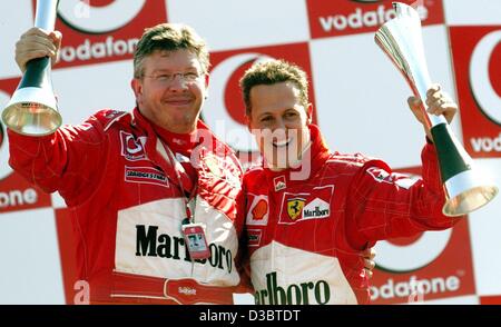 (Afp) - L'Allemand Michael Schumacher, pilote de formule 1 de Ferrari (R) et Ferrari directeur Ross Brawn (L) cheer et vague leurs trophées après Schumacher remporte le Grand Prix d'Italie à Monza, le 14 septembre 2003. Schumacher mène désormais au classement général avec 82 points. Banque D'Images