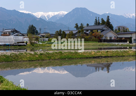 Paysage de montagnes enneigées du Japon sur les Alpes du Nord avec des maisons qui se reflètent dans des rizières inondées à Hotaka, Nagano, Japon Banque D'Images