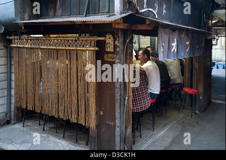 Les clients derrière le rideau noren profitez de la bonne nourriture et de l'amitié au comptoir eatery dans Omoide Yokocho, Memory Lane, Shinjuku, Tokyo Banque D'Images