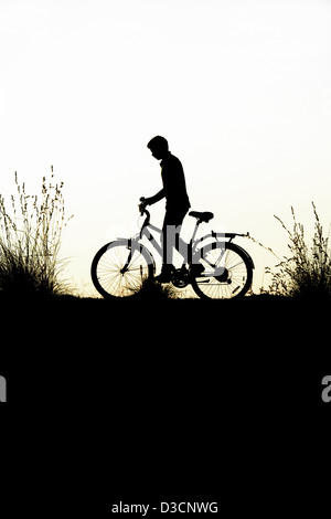 Indian boy riding bicycle parmi les graminées. L'Inde. Silhouette Banque D'Images