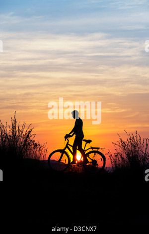 Indian boy riding bicycle parmi les graminées au coucher du soleil. Silhouette. L'Inde Banque D'Images