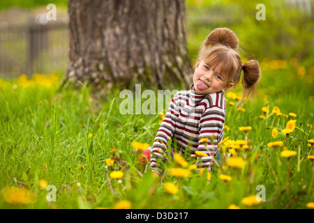 Jolie petite fille jouant dans le parc, affiche la langue (regardant la caméra) Banque D'Images