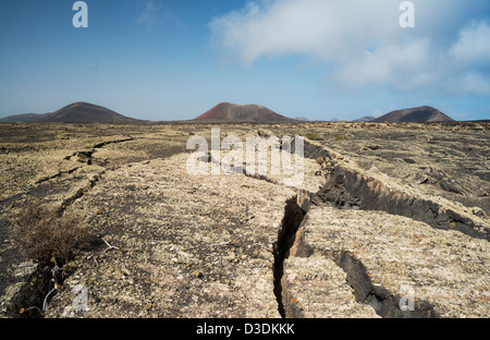 Fissurée, couverts de lichens de laves basaltiques près de Masdache, Lanzarote avec Montanas Negra, Colorada et Ortiz dans l'arrière-plan Banque D'Images