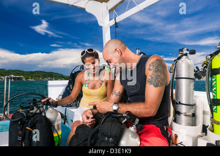 Deux plongeurs sous-plan de plongée d'examen et de vérifier l'équipement technique sur le bateau avant de commencer la plongée Tec. Roatan, Honduras Banque D'Images