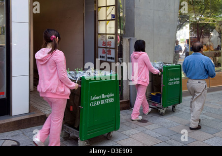 Les filles en rose jump suits pousser les ordures le long des chariots-dori haut de la rue commerçante Omotesando à Tokyo maintenant trottoir propre. Banque D'Images