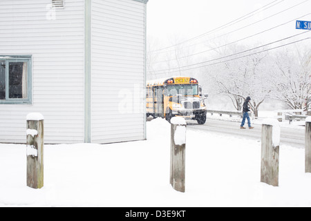 Un petit garçon traverse la rue en face d'un autobus scolaire dans une tempête de neige (alors que la lecture de ses messages téléphoniques). Banque D'Images