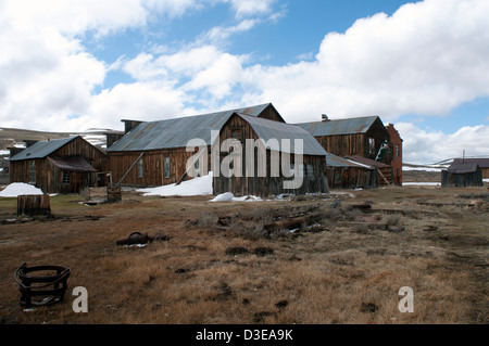 La neige autour des bâtiments historiques en bois de 'Ghost Town' sous ciel nuageux sur une journée froide à Bodie State Historic Park en Californie Banque D'Images