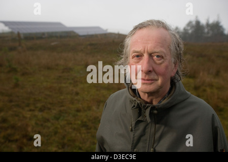 Île de Eigg, ÉCOSSE - 1er novembre 2007 : John Booth se trouve dans la pluie avec les banques de cellules solaires derrière lui. Banque D'Images