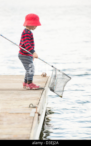 Les jeunes enfant debout sur un quai au bord de la mer en regardant l'eau avec filet de pêche dans la main Banque D'Images