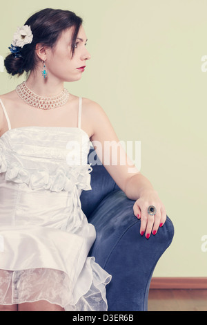 Une femme en robe blanche est assis sur un fauteuil bleu Banque D'Images