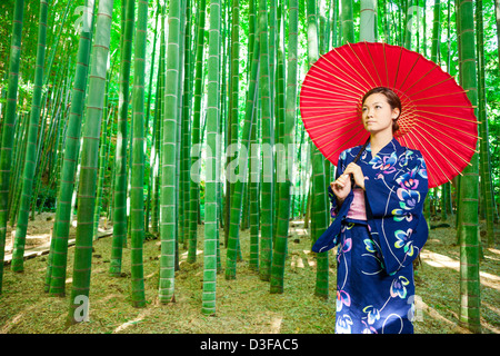 Japanese woman wearing kimono et holding red parasol est en bamboo grove Banque D'Images