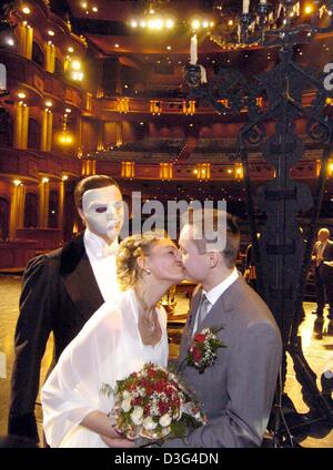 (Afp) - L'épouse Violetta Rogolowski (C) et le marié Andreas Schaefer (R) baiser pendant leur cérémonie de mariage dans le théâtre musical à Stuttgart-Moehringen, Allemagne, le 19 décembre 2003. Dans l'arrière-plan Ian Jon Bourg, qui joue le rôle du fantôme dans "Le Fantôme de l'opéra'. Rogolowski et Schaefer sont le premier couple à se marier sur la scène du théâtre. Banque D'Images